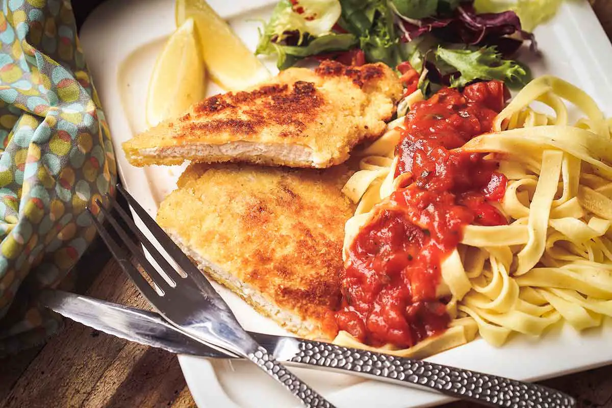 escalope milanaise servie avec des pates et une petite sauce tomate 