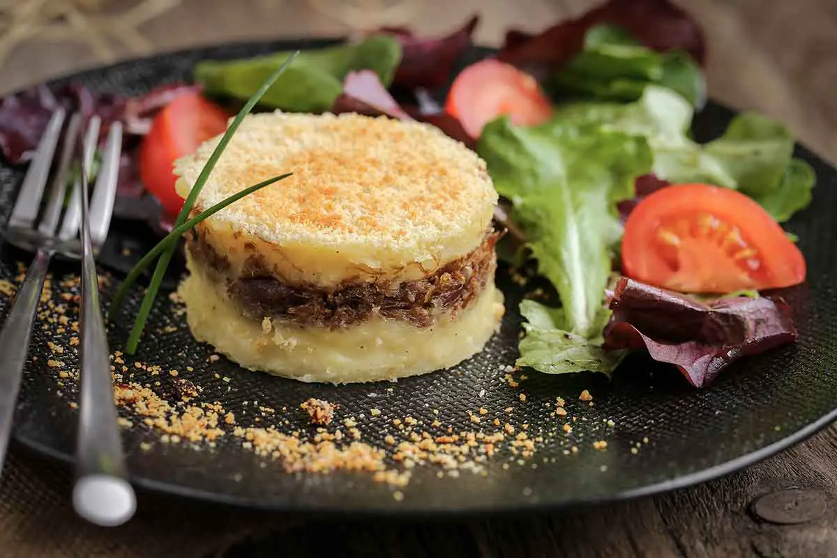 recette de hachis parmentier au confit de canard servi en assiette avec une petite salade composée